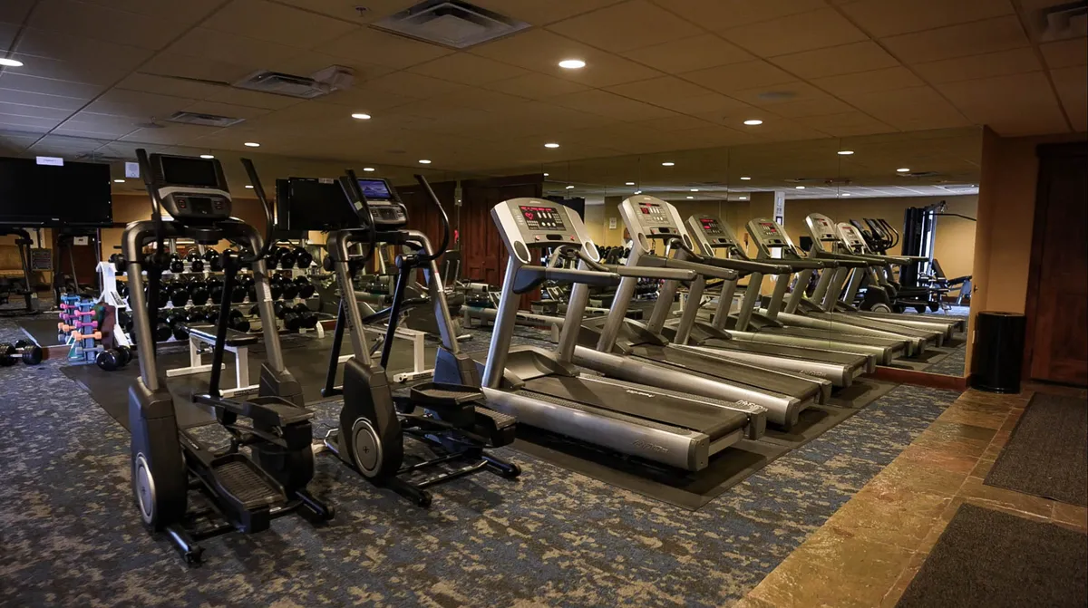 A well-equipped fitness center with treadmills, elliptical machines, dumbbells, and a mirrored wall, creating a motivating atmosphere for workouts and fitness routines.