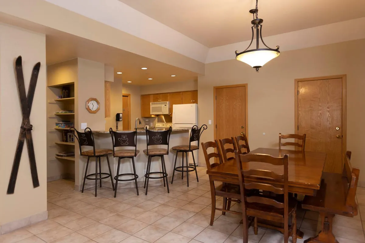 The dining area with a large table, bar stools at the kitchen counter, and decorative skis on the wall. The kitchen area is visible, creating a sense of openness and togetherness. The space is set up for shared meals, casual gatherings, and lively conversation.