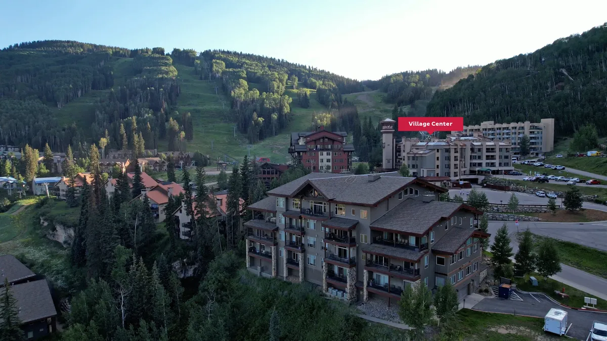 A wide shot of the Village Center with a majestic mountain backdrop, the Village Center sign, surrounding trees, and residential buildings nestled amidst nature, showcasing the resort’s vibrant setting.