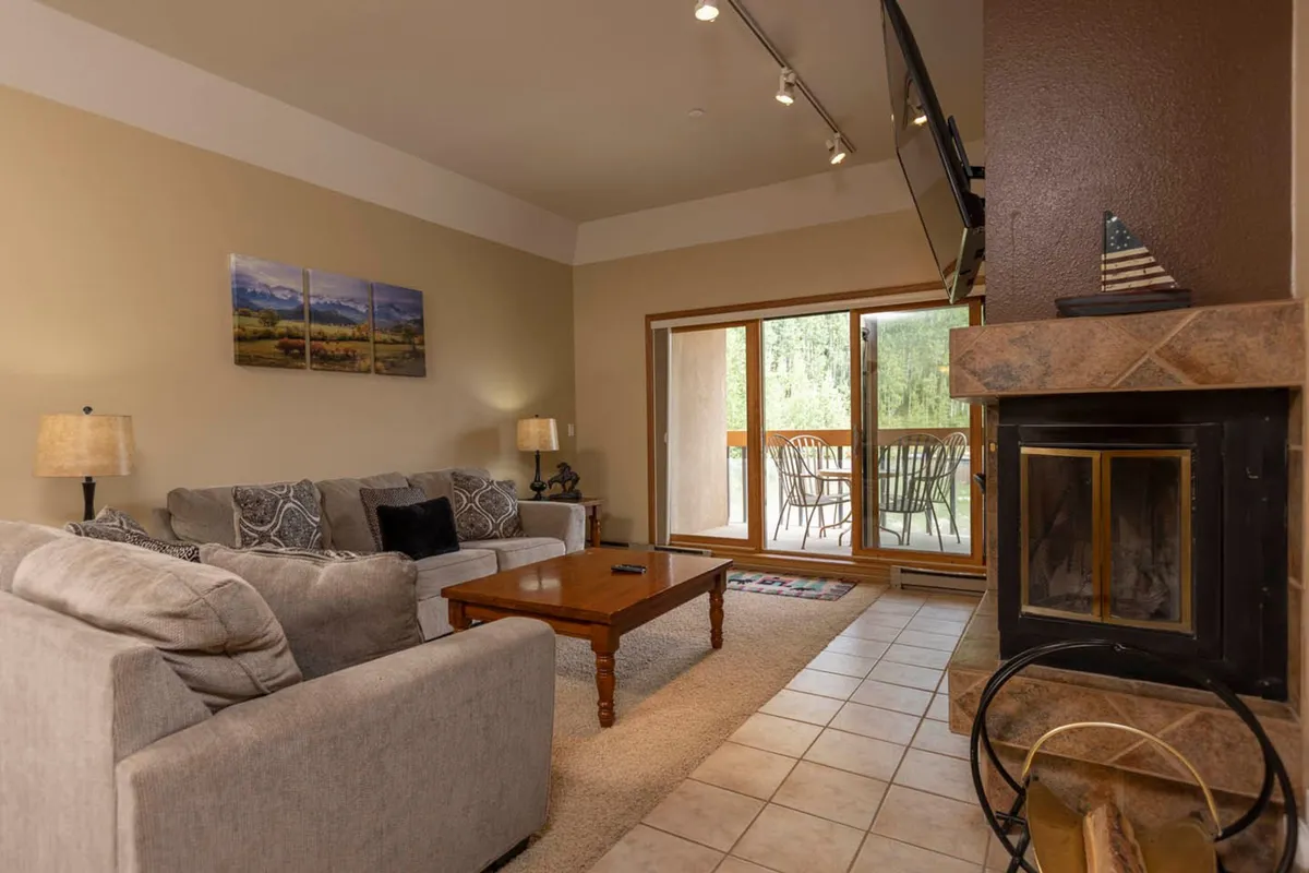 A cozy living room featuring a plush sofa, coffee table, fireplace, and a large window that frames a beautiful mountain sunset. Artwork on the wall adds a touch of personality and warmth, while the inviting seating area is perfect for relaxation or socializing after a day on the slopes.