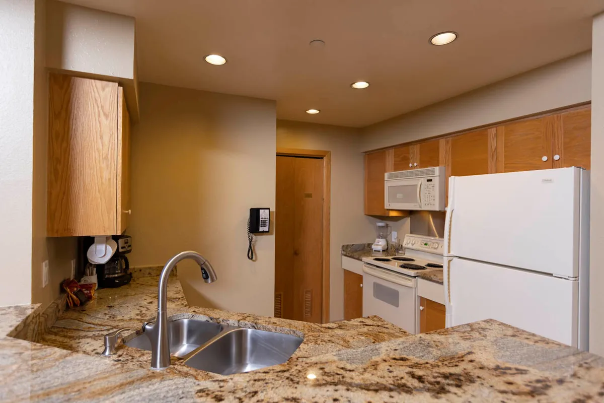 A stylish kitchen area, featuring a granite countertop, high-end kitchen appliances, and warm wood cabinetry. The space is open and welcoming, designed for both casual cooking and social gatherings, representing the comforts of a private condo.