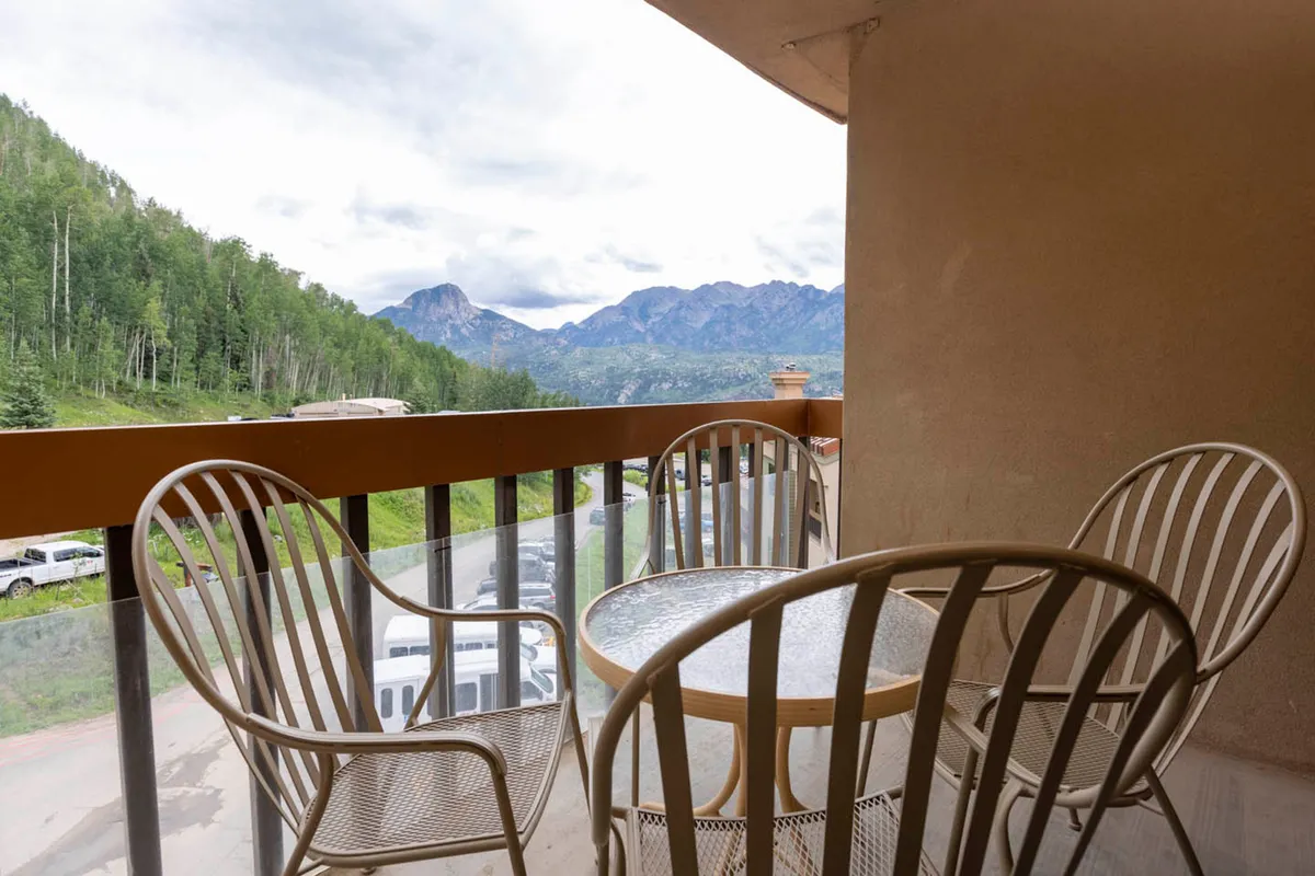 A private balcony outfitted with seating and a table faces an expansive mountain view, ideal for relaxing or socializing after a day on the slopes.