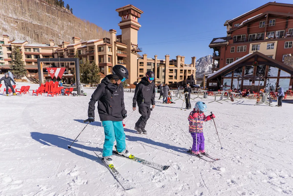 A vibrant, snowy exterior scene with skiers on the slopes, mountain backdrops, and resort buildings, capturing the thrill of ski-in/ski-out access and family fun in the snow.