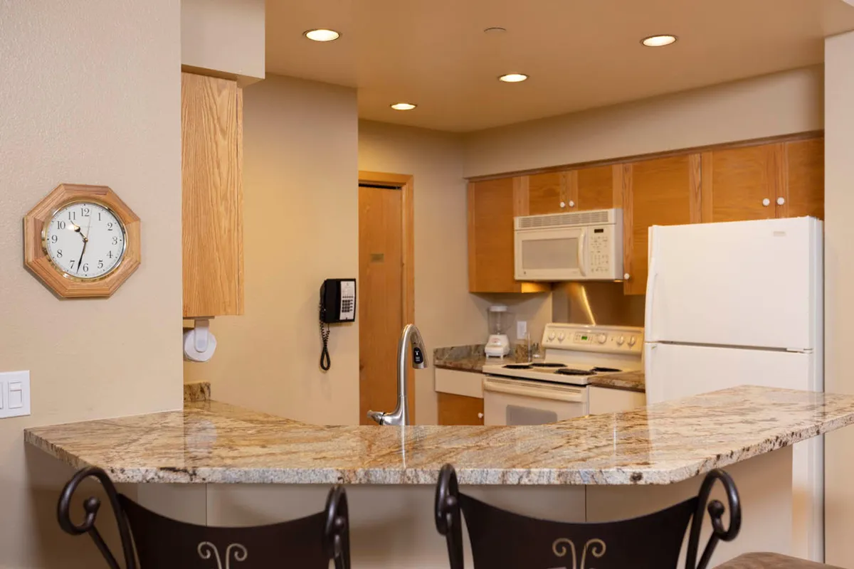 A welcoming kitchen scene with a granite countertop, modern appliances, bar stools, and a wall clock. The layout is perfect for family gatherings, cooking together, and sharing casual conversations, evoking togetherness and comfort.