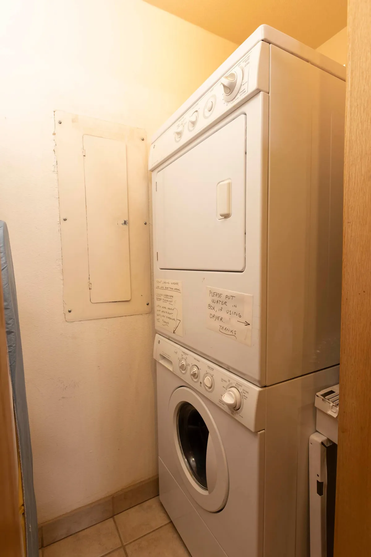 A bright, practical laundry facility featuring a stacked washer and dryer, with clear instructional notes visible on the wall. The setting is simple and functional, emphasizing ease of use for residents returning from outdoor activities.